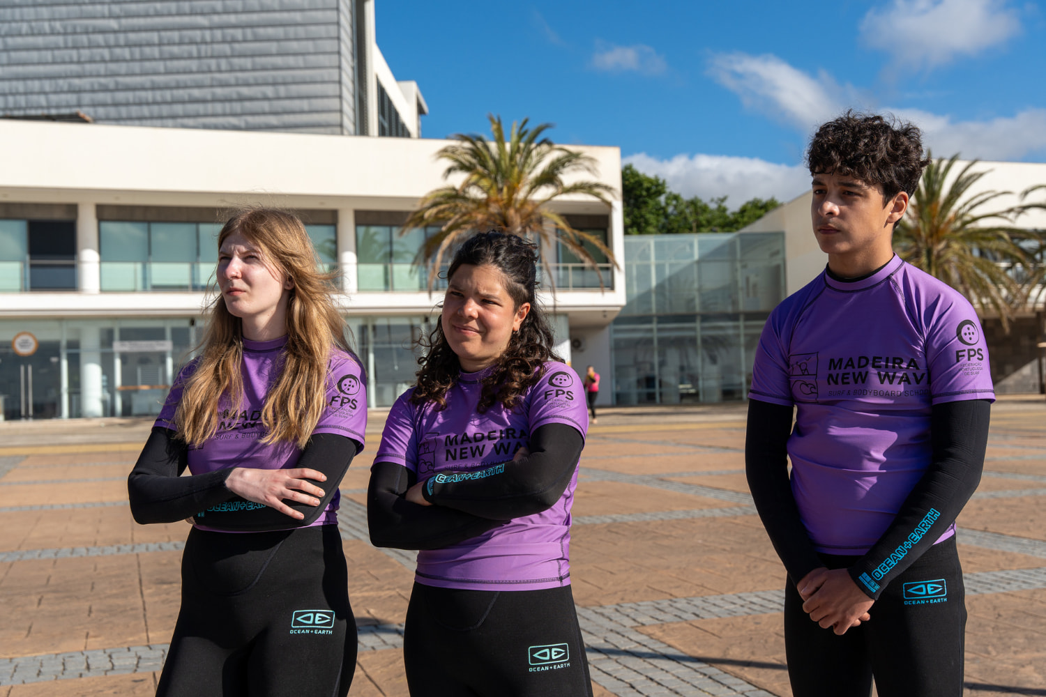 Group of three friends looking at the instructor while using their rented wetsuits in madeira
