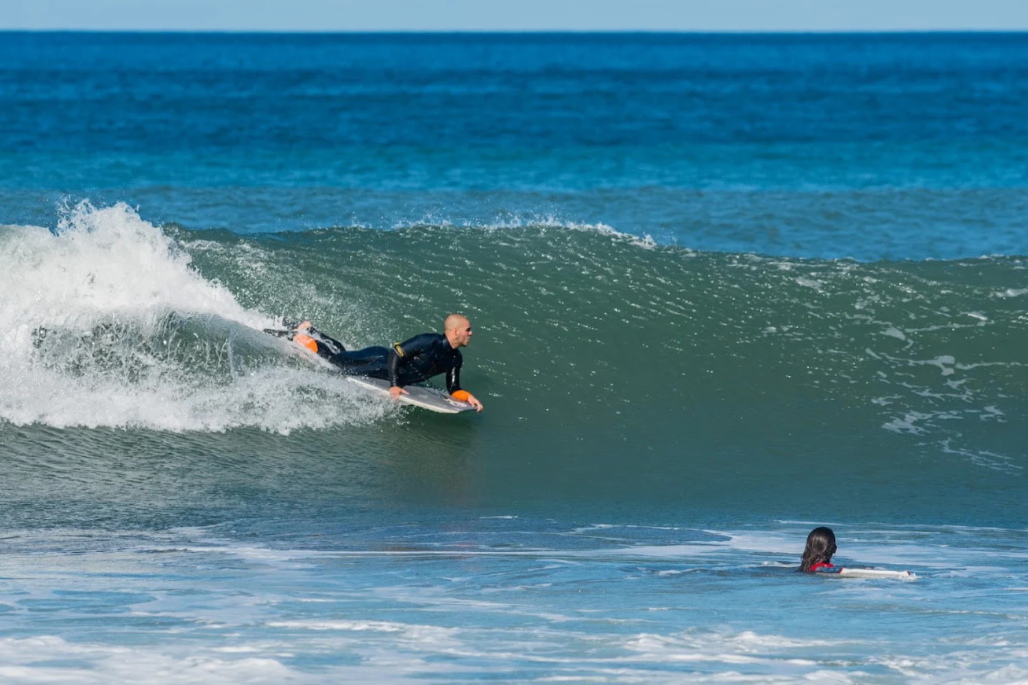 Male bodyboarder riding a wave in a sunny day while doing a group bodyboard lesson in machico
