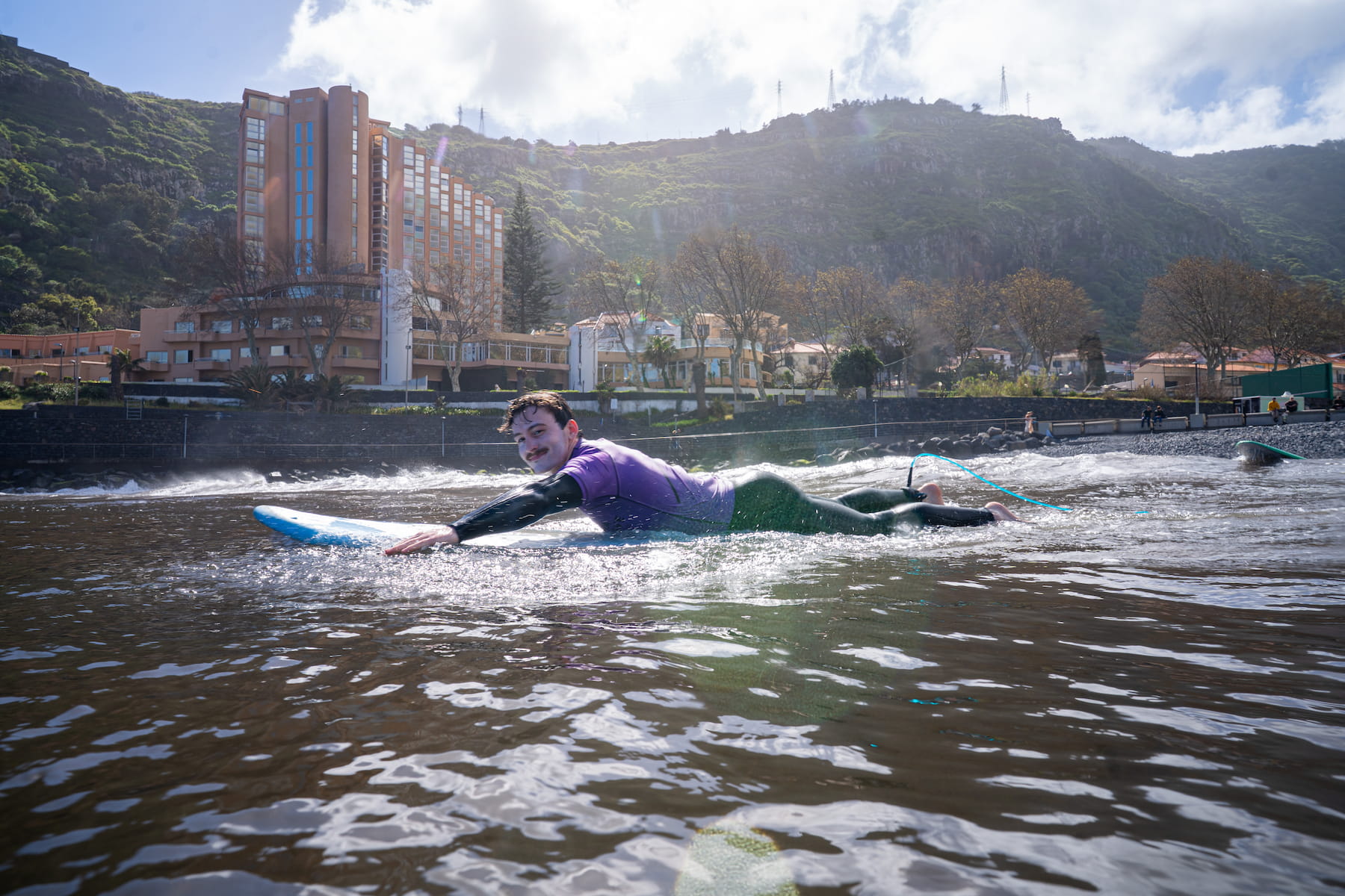 Male happy surfer laying in his surfboard while doing a surf lesson in machico and using his rented wetsuit in madeira